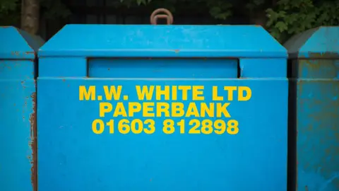 A blue paper bank with yellow writing which says M.W. WHITE LTD PAPER BANK with a phone number of the company. 