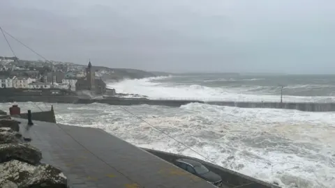 A sea view from Porthleven in Cornwall. The waves are crashing against the breakwater and buildings.
