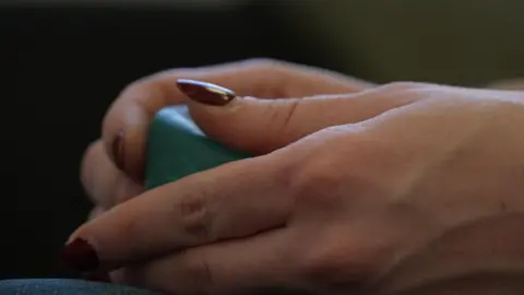BBC La imagen muestra manos con uñas pintadas de color burdeos sosteniendo un cubo de color verde azulado en sus manos.