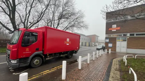 Red Royal Mail post lorry exits the Delivery Office at Yate