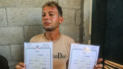 Getty Images Palestinian father Mohammed Abu al-Khumsan holds up the birth certificates of his twins.