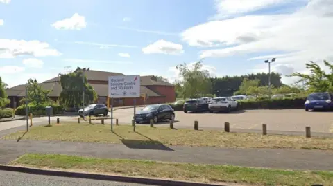 Google Entrance to leisure centre with "Redwell Leisure Centre and 3G Pitch" sign in the foreground.  There is a car park behind the sign and a two-storey brick building to the left, flanked by trees