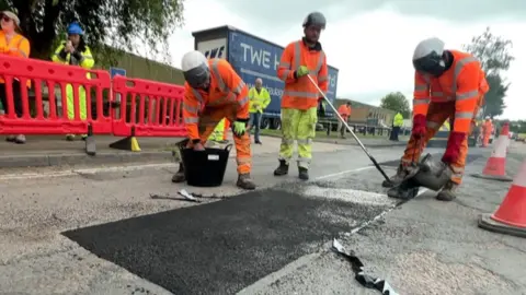 Contractors in hi-vises and hard hats repair a pothole in Banbury.
