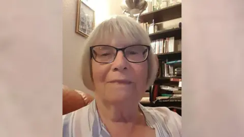 Durham Police Janet Holmes with grey hair in a bob and black glasses. She is wearing a white striped shirt. She is looking at the camera. 