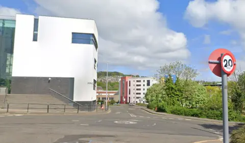 Google A mini roundabout with a 20 mph traffic sign and a white building in the foreground 