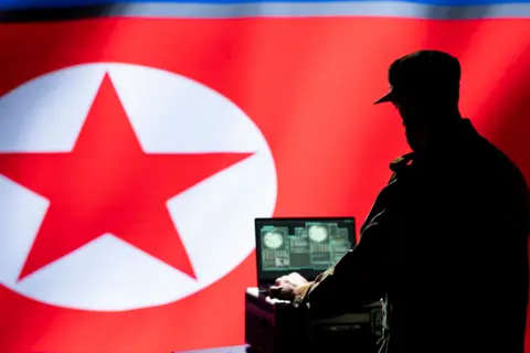 Getty image showing a man wearing a hat and working on a laptop with a North Korean flag