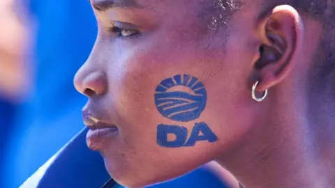 Getty Images A black woman at a rally with the DA logo stamped on her face.