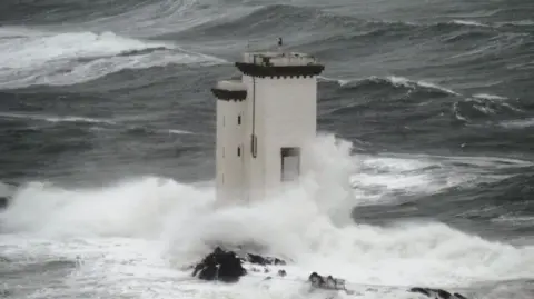 livvy/BBC Weather Watchers A lighthouse is buffeted by waves.
