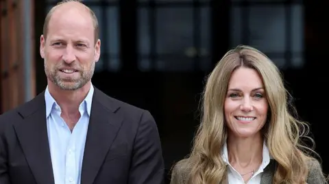 Getty Images Shoulder crop of William and Catherine. William is wearing a black blazer and light blue shirt. Catherine is wearing a tweed-style jacket and white shirt. She has blonde hair. Both are smiling and posing outside the museum.