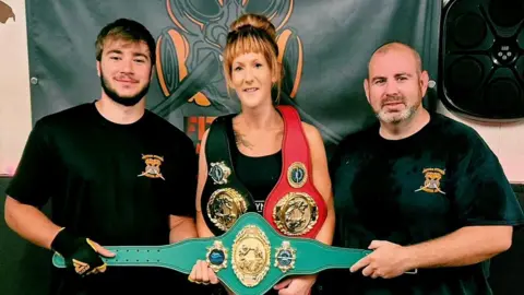Andrew Takle Lucy Payne holding teal belt with two men stood either side. 