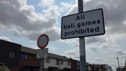 Vanessa Clarke/BBC Two signs are on a residential street lined with houses. One reads 'All ball games are prohibited'. The other says 'Play Street 8am to sunset except for access'.