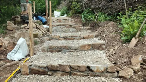 Heidelberg Materials Gorge Walk improvements at Cheddar Gorge showing new steps up a slope being constructed from rock and wood