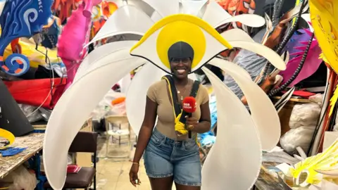 Aminata Kamara smiles astatine  the camera whilst wearing a flowery carnival costume