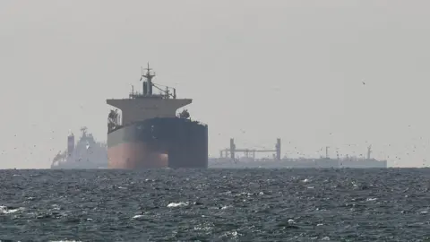 Reuters Tanker sails on open sea in the Gulf near the Strait of Hormuz, while several other ships are silhouetted in the background behind it