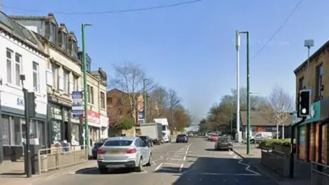 A street in Bradford. It is busy with cars, with shops and restaurants on both sides of the street. 