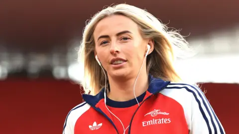 Chloe Kelly wearing headphones and an Arsenal training top