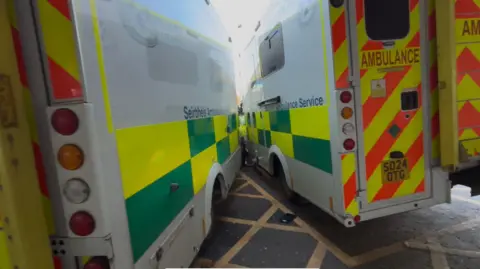 The two ambulances pictured from behind with the front of the vehicles smashed together