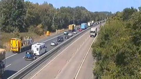 National Highways A blurry traffic camera shows stationary traffic on one side of the M54. It's a sunny and clear day.