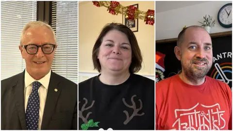BBC Three individuals standing side by side in separate frames. The first person is Mike Powell, wearing a dark suit with a white shirt and a patterned tie, standing in front of a window with blinds. The second person is Charlotte Riley dressed in a black sweater featuring reindeer antlers and a green bow design, with festive garland visible in the background. The third person is Richard Nunn, wearing a red graphic T-shirt, with holiday decorations and a clock on the wall behind.