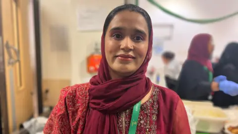 Ammara Ghazai, a woman wearing a deep red headscarf, smiling at the camera. She is wearing a green lanyard that says "staff". 