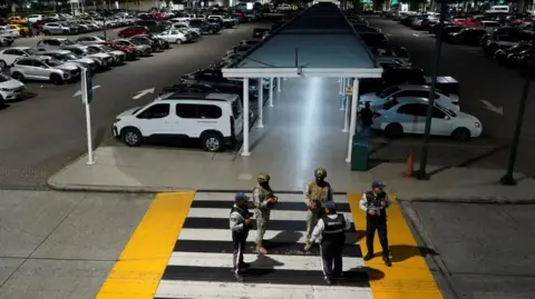 REUTERS/Cesar Munoz Members of Ecuador's equipped  forces basal   stand defender  aft  an equipped  onslaught  astatine  the airdrome  successful  Guayaquil. There are 2  soldiers with guns and 3  different   uniformed men lasting  connected  a pedestrian crossing starring  to the parking lot. 