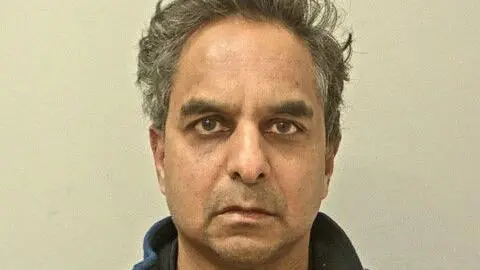 Police mugshot of Dr Amal Bose. He has short, unkempt dark hair that is greying and is looking directly at the camera, frowning slightly. He has brown eyes and bushy eyebrows.
