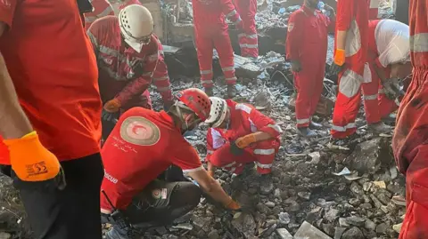 EPA A handout photo made available by Iranian Red Crescent Society (IRCS) shows rescuers working at the site of an airstrike on a residential area in Tehran. Many men wearing red uniforms dig through rubble.