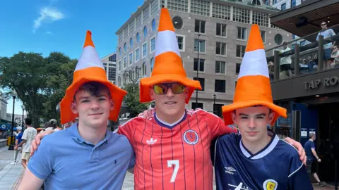 A man and his two sons either side of him - all three are wearing traffic cone hats