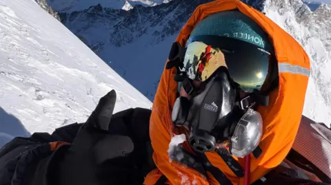 Michael Woods Michael Woods is standing on the side of a snow-covered mountain. He is wearing a High-altitude breathing, a coat with hood up, sunglasses and a hat. 