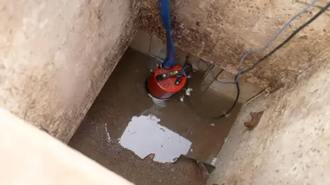 A red pump inside a concrete shaft with water and sand