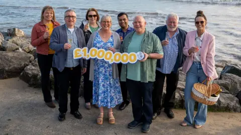 The National Lottery A group of men and women celebrating on a beach with a £1,000,000 sign 