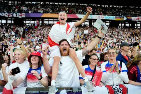 Nick Potts/PA wire A young girl draped in an England flag sits on a man's shoulder surrounded by cheering England fans in a packed stadium
