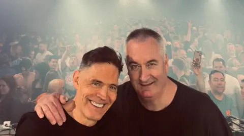 Soma Records Two men in black t-shirts smile in front of a large crowd in a Glasgow nightclub