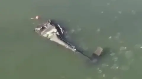 A crashed Army helicopter lies on its side in the Potomac river.