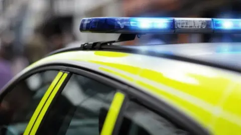 A close-up photo of a yellow police car with a blue light on the top