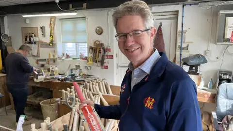 BBC Gray-Nicolls CEO Richard Nicolls holding a cricket bat in the factory workshop surrounded by cricket bats