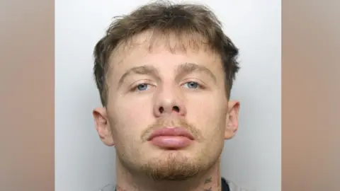A police mugshot of Billy Mole, who has short blonde hair and neck tattoos.