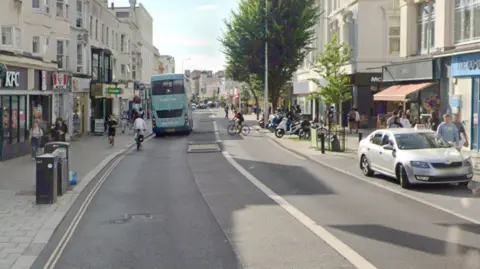 A Google Street map image of a road with high street shops either side.