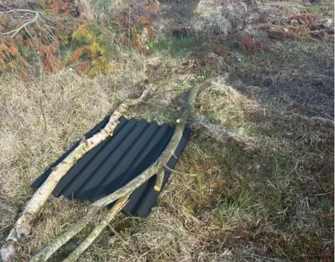 Forestry and Land Scotland A black metal sheet held down by two long sticks on green grass