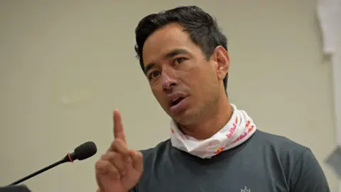 Nirmal Purja speaking into a microphone, with one finger raised