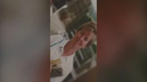 Blurred and old photo of a woman wearing a white shirt and holding a newspaper. She has dark blonde hair.