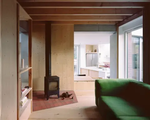 Building Narratives Wooden interior of six columns with fireplace and green sofa