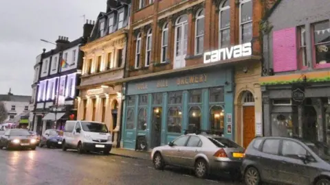 Mike Faherty An illuminated sign bears the word "Canvas" above a bar on a street at dusk