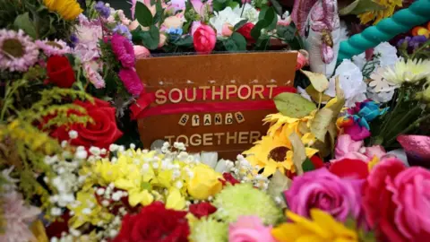 PA's media flowers left by the public after the deadly knife attack in Soutbort. In the middle is a sign of read: "Southport stands together".