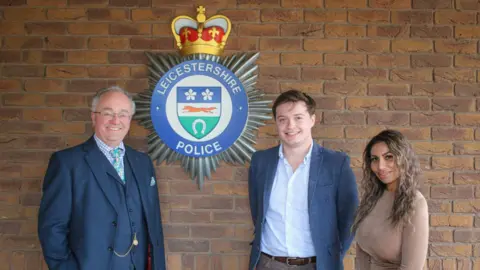 Leicestershire Police and Crime Commissioner's office Two men and a woman standing by a police crest mounted on a wall