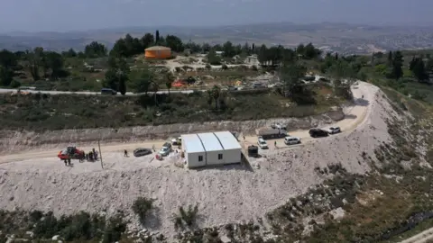 An aerial view shows people around a portable building under construction at the illegal Israeli settler outpost of Homesh, near the Palestinian village of Burqa, in the occupied West Bank (29 May 2023)