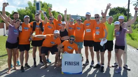 The team at the finish line in Antigua last year, wearing a mixture of orange and purple t-shirts and all in black running shorts.