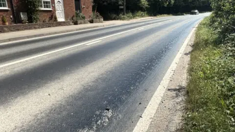 A road where there are dark patches of tarmac that have been melting in extreme heat.