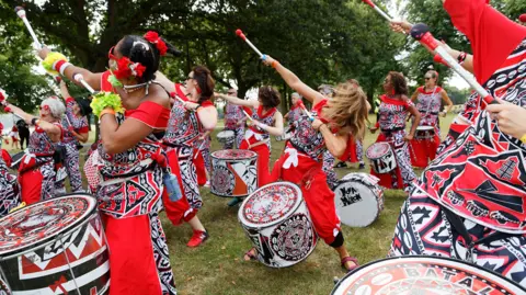 Leicester Caribbean Carnival Women dressed in red, black and white costumes performing while playing drums at Leicester Caribbean Carnival