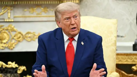 President Donald Trump wearing a blue suit and red tie, talks to reporters.